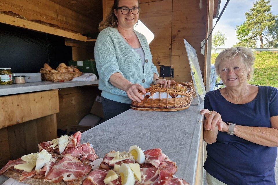 Eine Verkäuferin bietet frische Fleischwaren in einem Holzstand an. Eine Kundin steht lächelnd daneben und genießt die Atmosphäre. | © Camping Resort Riegersburg