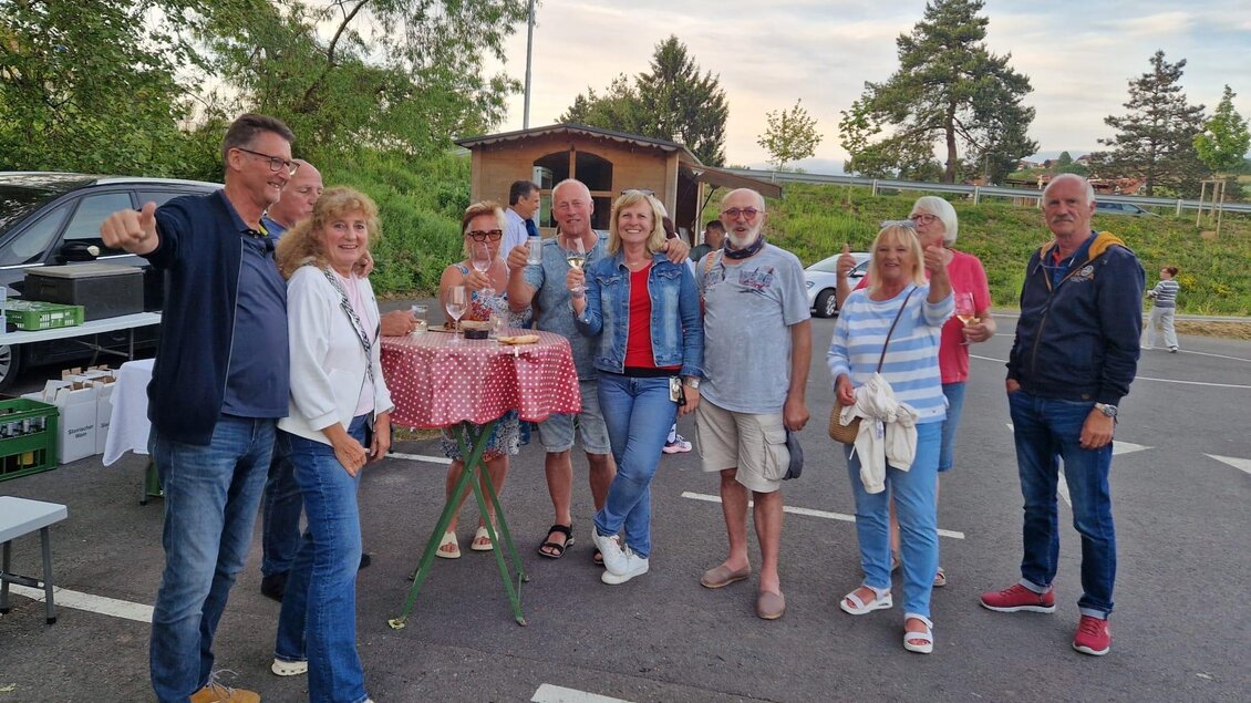 Eine Gruppe von Menschen steht auf einem Parkplatz und lächelt. Sie halten Getränke in der Hand und scheinen eine fröhliche Zeit zu haben. | © Camping Resort Riegersburg