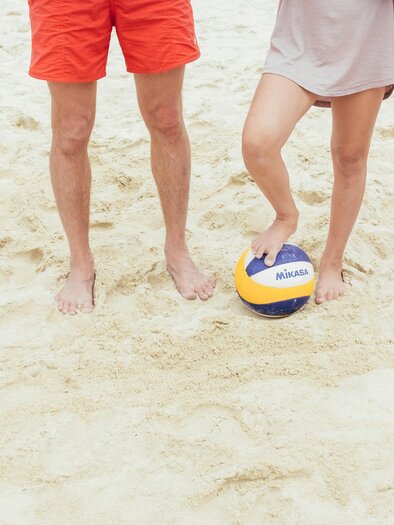 Vier Personen stehen barfuß auf einem sandigen Strand. Eine Person hält einen Volleyball zwischen ihren Füßen. | © Thermenresort Loipersdorf