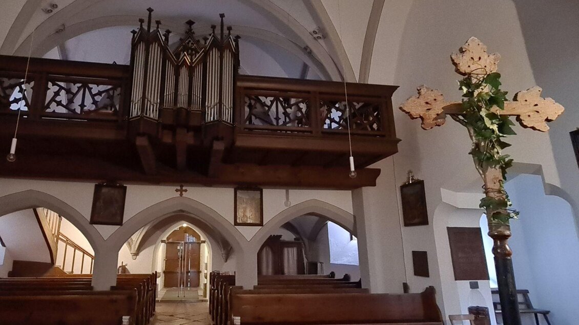Eine ruhige Kirche mit einer Holzempore und einer Orgel. Holzene Bänke und eine atmosphärische Beleuchtung schaffen eine besinnliche Stimmung. | © Stephanie Bor