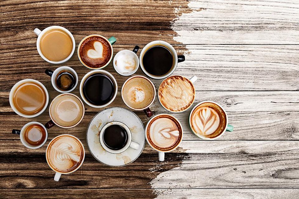Eine Vielzahl von Kaffeetassen auf einem Holztisch. Einige Tassen haben kunstvolle Milchschaummuster. | © Bild: freepik