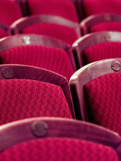 Red theater chairs arranged in rows. The chairs have soft cushioning and an elegant wooden covering. | © Pixabay