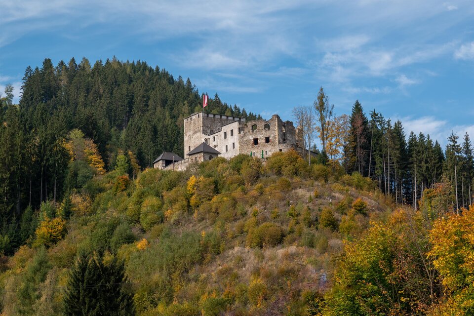 Eine alte Burg steht auf einem Hügel, umgeben von Bäumen und farbenfrohen Herbstblättern. Der Himmel ist klar und blau. | © TV Hochsteiermark, Hans Schrotthofer