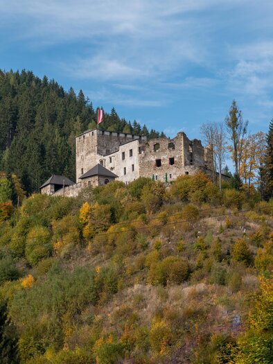 Eine alte Burg steht auf einem Hügel, umgeben von Bäumen und farbenfrohen Herbstblättern. Der Himmel ist klar und blau. | © TV Hochsteiermark, Hans Schrotthofer