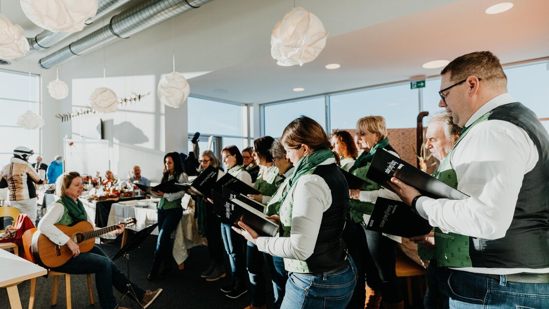 Eine Gruppe von Sängern singt in einem modernen Raum. Eine Person spielt Gitarre, während die anderen das Lied begleiten. | © nicoleseiser.at