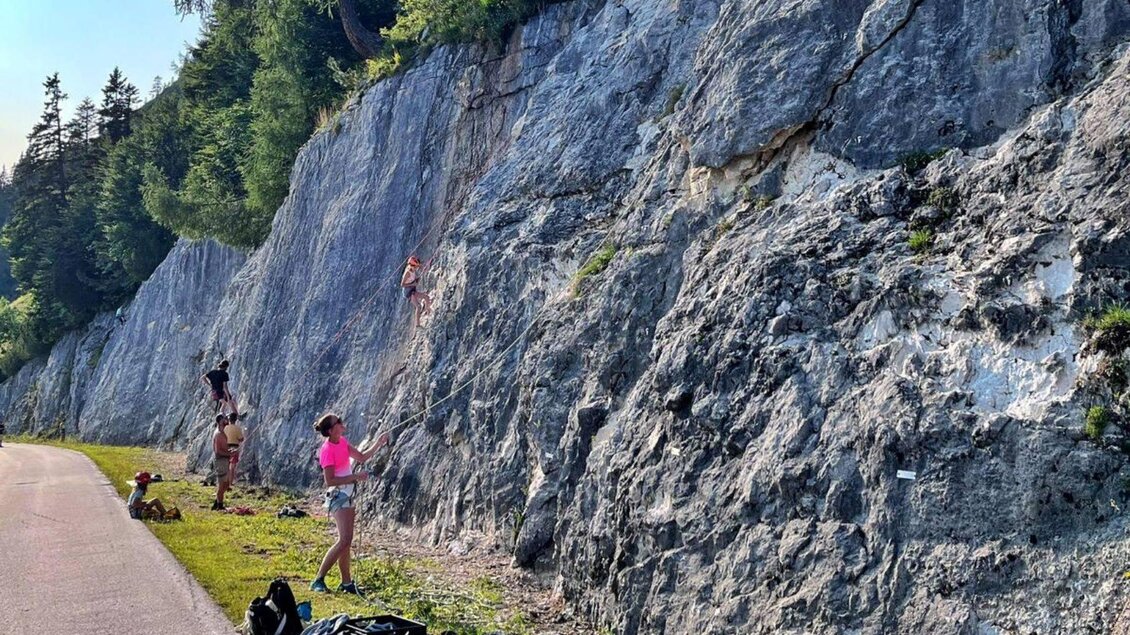Ein Felsen mit Kletterern, die an einer Wand Höhenmeter überwinden. Im Vordergrund sind einige Personen und Ausrüstung zu sehen. | © Loser Bergbahnen
