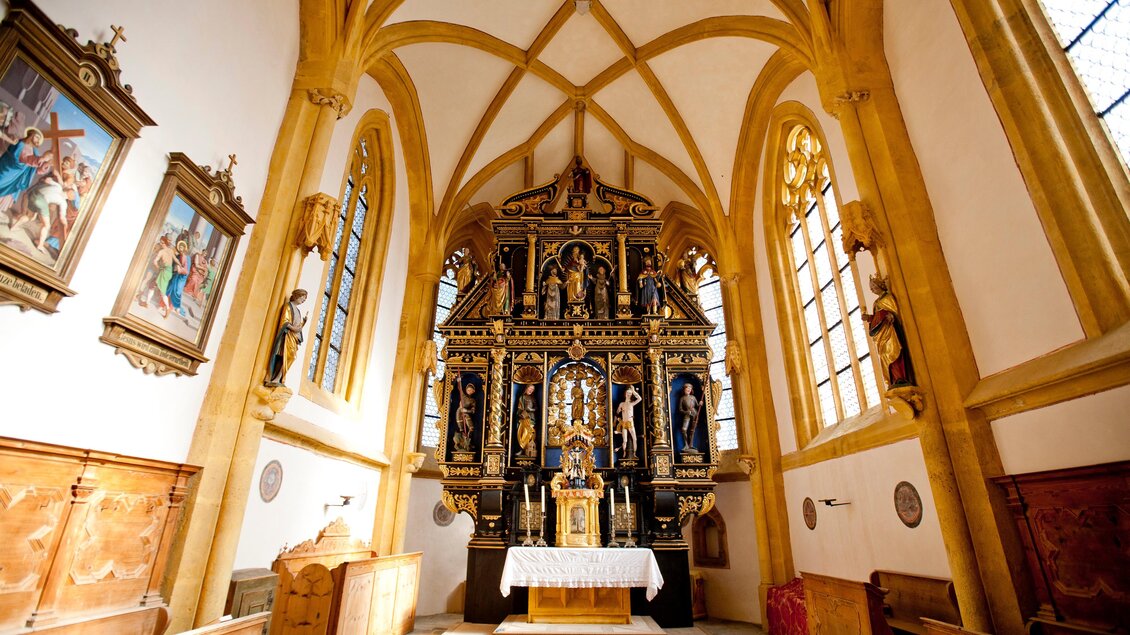 Eine schmuckvolle Kirche mit einem kunstvollen Altar im gesperrten Design. Helle Fenster und Holzdecken verleihen dem Raum eine warme Atmosphäre.
