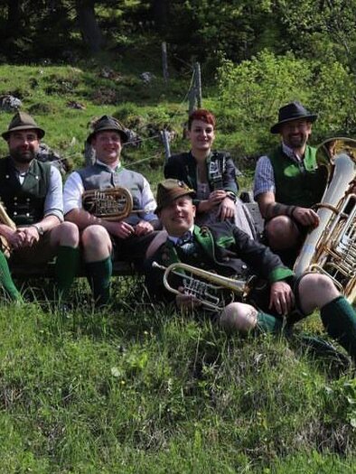 The musicians from D'Röthelstoana in traditional attire with their instruments of classical folk music are sitting on a summer meadow in the Ausseerland. | © Das Schutzhaus / D'Röthelstoana