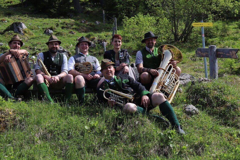 Die Musikanten von D'Röthelstoana in traditioneller Tracht  mit ihren Instrumenten der klassischen Volksmusik sitzen auf einer sommerlichen Wiese im Ausseerland.  | © Das Schutzhaus / D'Röthelstoana