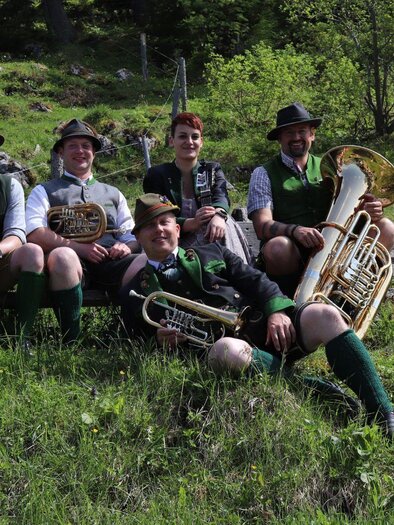The musicians from D'Roethelstoana in traditional attire with their instruments of classical folk music sit on a summer meadow in Ausseerland. | © Das Schutzhaus / D'Röthelstoana