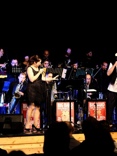 Eine Sängerin steht am Mikrofon und singt, während eine Band im Hintergrund spielt. Sie trägt ein elegantes schwarzes Kleid und zeigt Freude beim Auftritt. | © Tourismusverband Oststeiermark