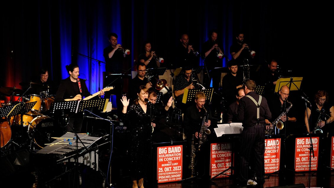 Eine Big Band spielt auf einer Bühne mit verschiedenen Instrumenten. Die Musiker sind in schwarzer Kleidung und die Atmosphäre ist lebhaft mit bunten Lichtern. | © Tourismusverband Oststeiermark