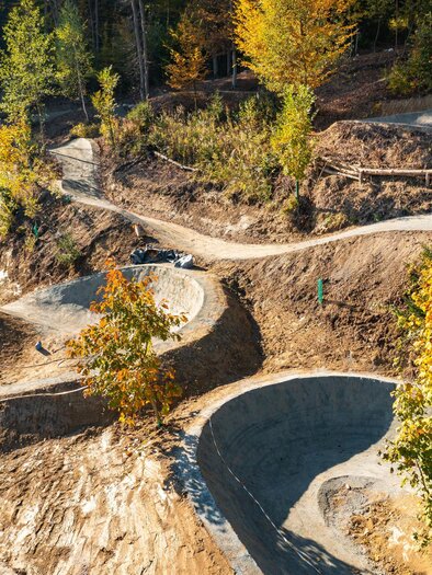 Eine kurvenreiche Bike-Strecke in einer herbstlichen Umgebung. Bäume und gelbe Blätter umgeben den Weg aus Schotter. | © Petru Rimovetz