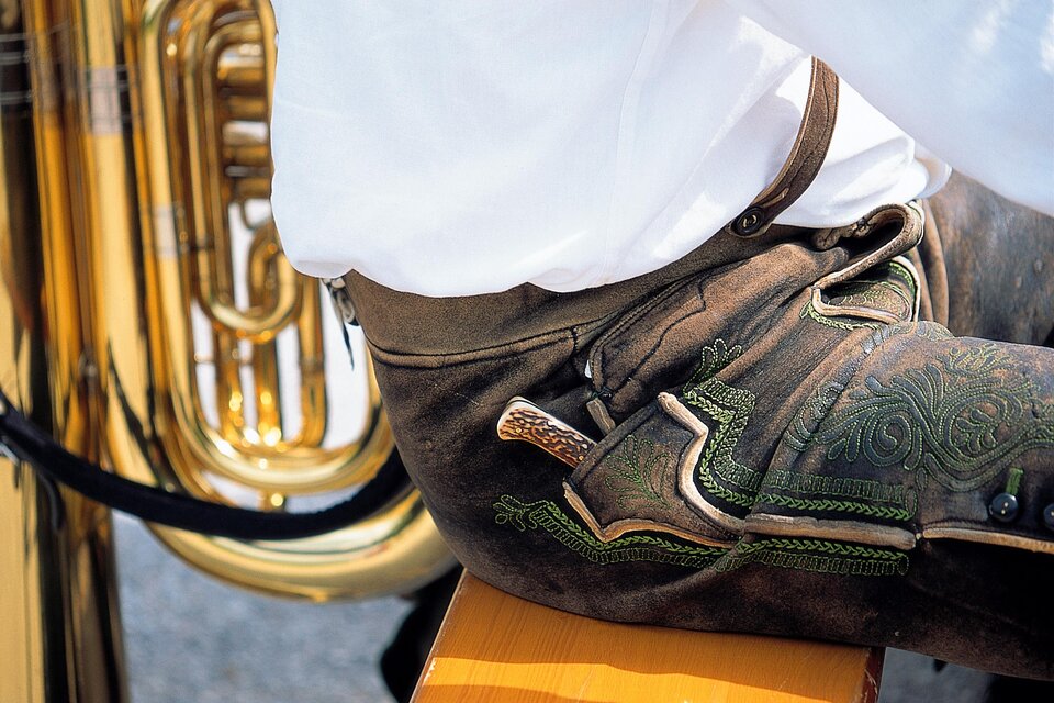 Ein Musiker sitzt neben einer glänzenden Tuba. Er trägt traditionelle Lederhosen und ein weißes Hemd. | © Steiermark Tourismus-Reinhard Lamm