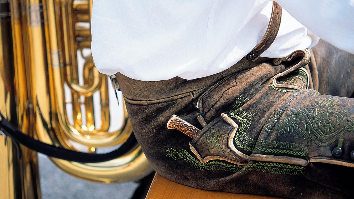 Ein Musiker sitzt neben einer glänzenden Tuba. Er trägt traditionelle Lederhosen und ein weißes Hemd. | © Steiermark Tourismus-Reinhard Lamm