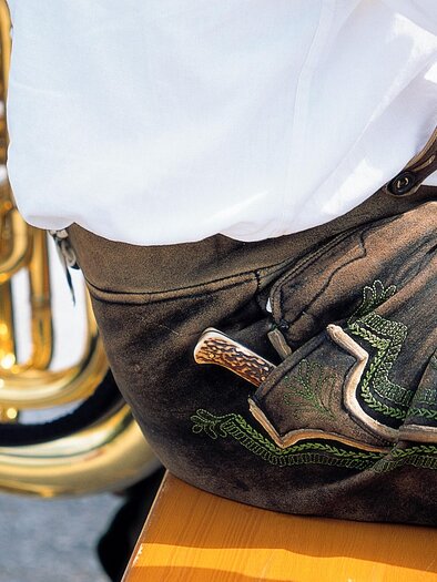 Ein Musiker sitzt neben einer glänzenden Tuba. Er trägt traditionelle Lederhosen und ein weißes Hemd. | © Steiermark Tourismus-Reinhard Lamm