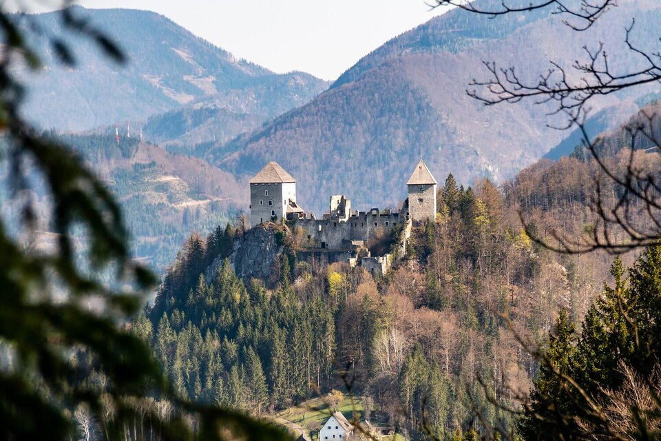 Eine alte Burg thront auf einem Hügel, umgeben von sanften Bergen. Der Wald darunter ist in frühlingshaften Farben erleuchtet. | © Christian Scheucher