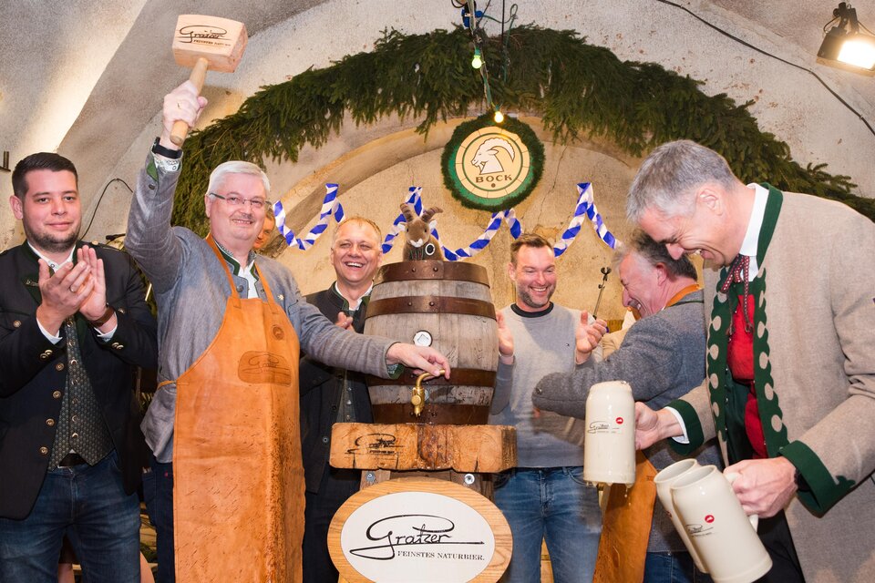 Eine Feier in einem Festsaal, bei der ein Bierfass angezapft wird. Die Teilnehmer tragen traditionelle Kleidung und zeigen Freude. | © Matthias Pöltl