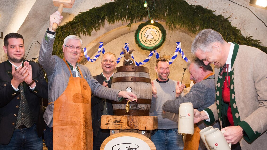 Eine Feier in einem Festsaal, bei der ein Bierfass angezapft wird. Die Teilnehmer tragen traditionelle Kleidung und zeigen Freude. | © Matthias Pöltl