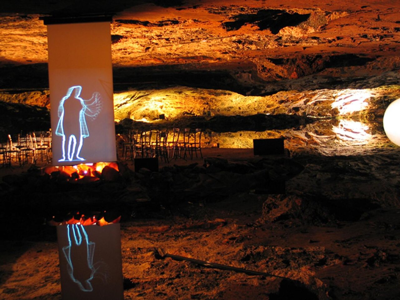 Eine unterirdische Höhle mit beleuchtetem Felsen und einem großen weißen Ball. An der Wand ist eine Projektion einer Figur zu sehen, die eine künstlerische Atmosphäre schafft. | © Rastl