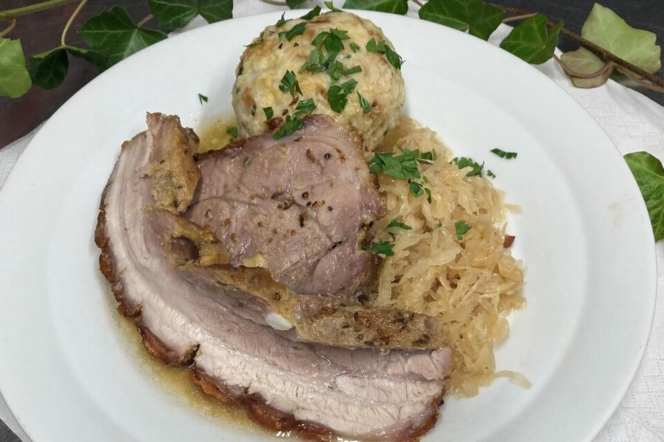 Ein Teller mit saftigem Schweinebraten, serviert mit Sauerkraut und einem Knödel. Das Gericht ist mit frischer Petersilie garniert. | © Popp'n Angerl, Familie Heiß