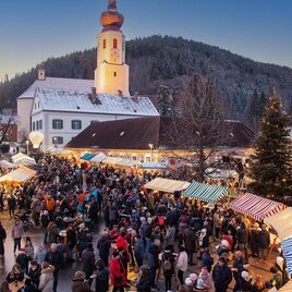 Ein belebter Weihnachtsmarkt mit zahlreichen Besuchern. Bunte Stände und eine Kirche im Hintergrund gestalten die festliche Atmosphäre. | © Robert Hahn