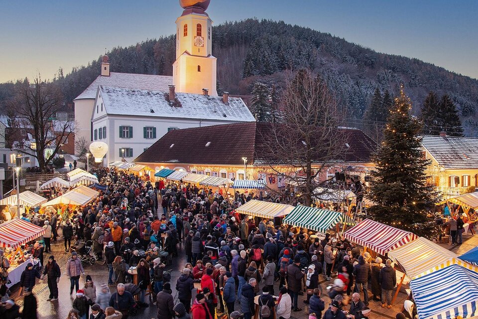 Ein belebter Weihnachtsmarkt mit zahlreichen Besuchern. Bunte Stände und eine Kirche im Hintergrund gestalten die festliche Atmosphäre. | © Robert Hahn