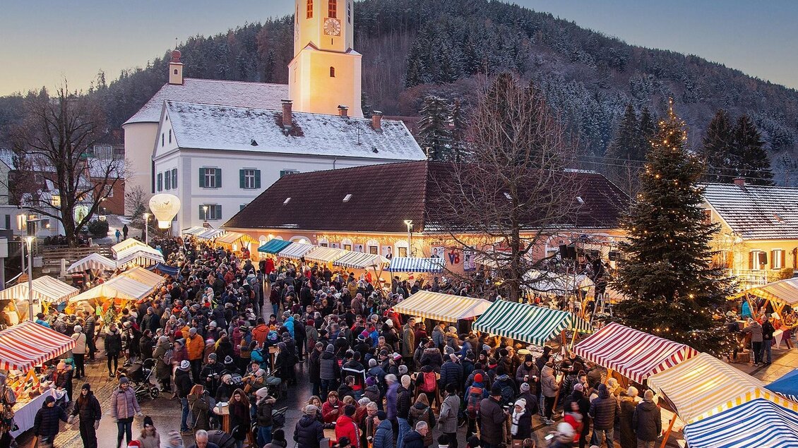 Ein belebter Weihnachtsmarkt mit zahlreichen Besuchern. Bunte Stände und eine Kirche im Hintergrund gestalten die festliche Atmosphäre. | © Robert Hahn