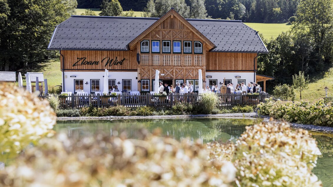Ein charmantes Holzhaus mit einem großen Garten und einem Teich. Die Umgebung ist grün und lädt zum Entspannen ein. | © www.zloamwirt.at