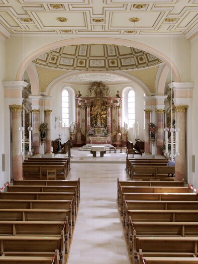 Eine ruhige Kirche mit Holzbänken und buntem Altar. Der Raum ist hell erleuchtet und zeigt kunstvolle Details an Wänden und Decke. | © Pixabay