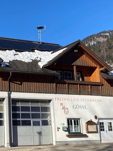 A beautiful, rustic building with wood siding and garage doors that serves as a fire station. In the background, snow-covered mountains and a clear blue sky can be seen. | © Bettina Scheck