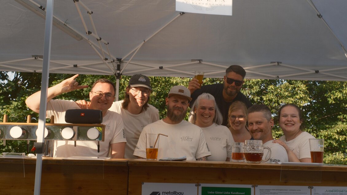 Mitglieder des Hobby-Bier-Brau-Vereins stehen mit Biergläsern gemeinsam hinter ihrem Stand in St. Bartholomä. | © Hobby Bier-Brau Verein