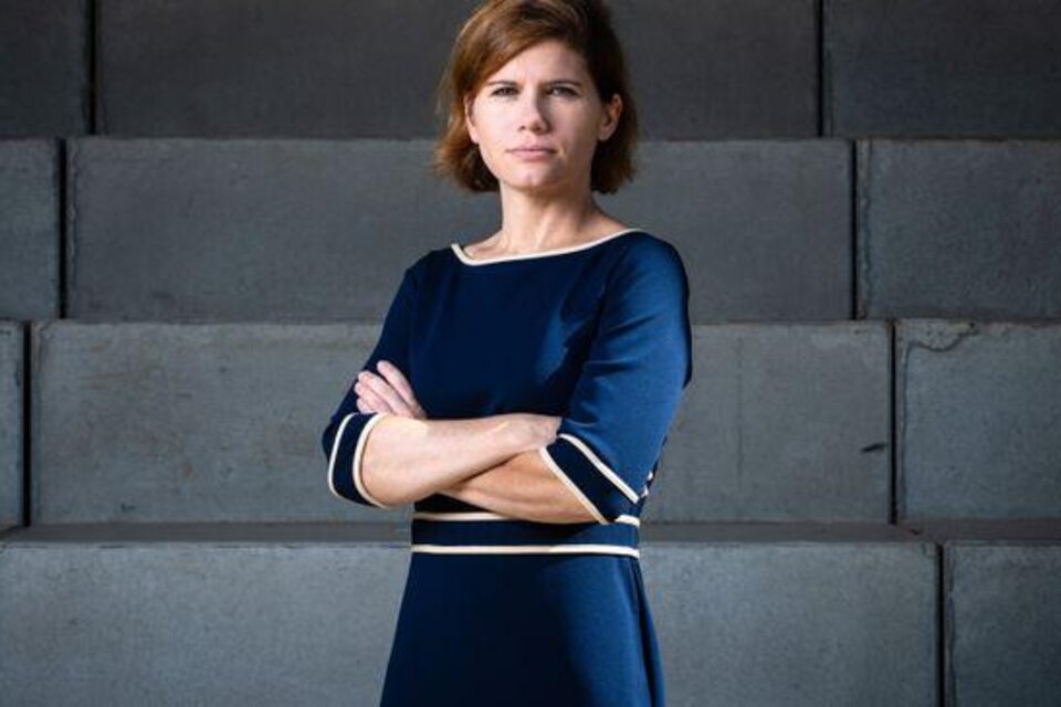 Eine Frau in einem blauen Kleid steht mit verschränkten Armen vor einer grauen Wand. Ihr Blick ist ernst und sie strahlt Selbstbewusstsein aus. | © Gianmaria Gava