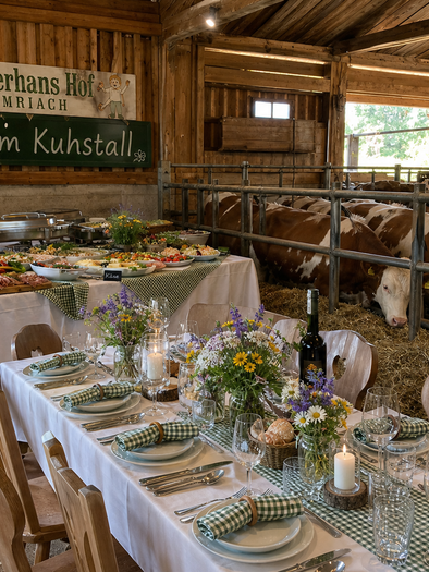Buffet and set table in the cowshed with cows at the Schusterhans farm in Semriach. | © ChatGPT-christine rotschädl