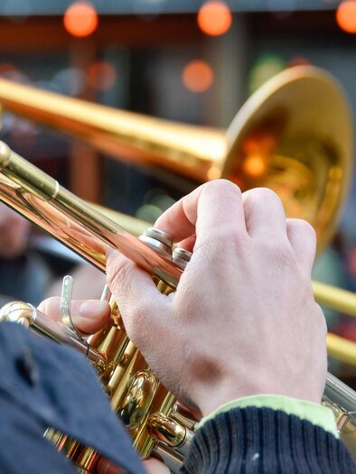 A musician is playing the trumpet. In the background, blurred people and lights can be seen. | © pixabay.com