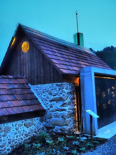 Ein modernes Haus mit Holz- und Steinelementen, das von einem sanften blauen Licht erleuchtet wird. Die Architektur kombiniert traditionelle und zeitgenössische Stile. | © Die Amtmann