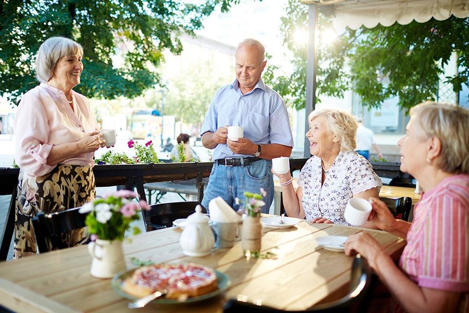 Eine Gruppe von Personen sitzt an einem Tisch in einem Café und genießt eine fröhliche Unterhaltung. Es ist sonnig und die Umgebung wirkt einladend und gemütlich. | © Bild: Freepik