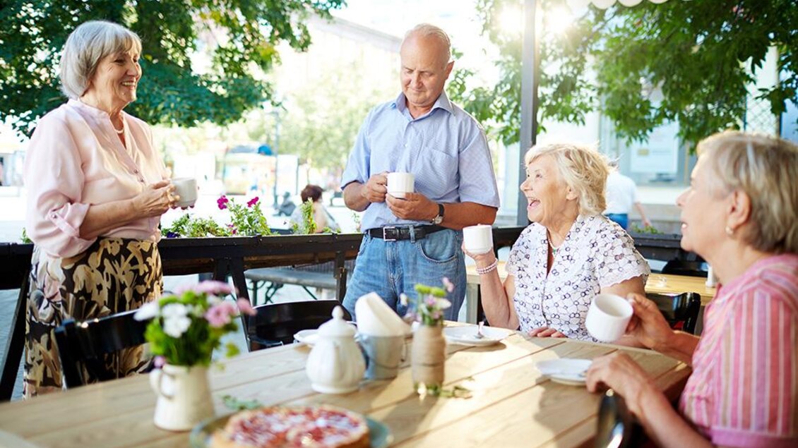 Eine Gruppe von Personen sitzt an einem Tisch in einem Café und genießt eine fröhliche Unterhaltung. Es ist sonnig und die Umgebung wirkt einladend und gemütlich. | © Bild: Freepik