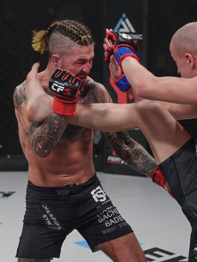 Zwei Kämpfer im Oktagon während eines MMA-Matches. Der Kämpfer mit geflochtenem Haar trifft seinen Gegner mit einem hohen Kick. | © Bobipix