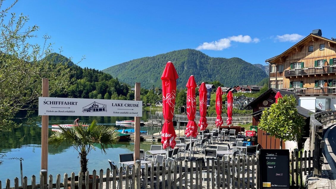 <p>Vom Eingang zur Seelaube in Grundlsee kann auf die Terrasse des Strandcafés gesehen werden. Im Hintergrund ist die Schiffsanlegestelle der Schifffahrt Grundlsee beim Seehotel zu sehen.</p> | © TVB Ausseerland