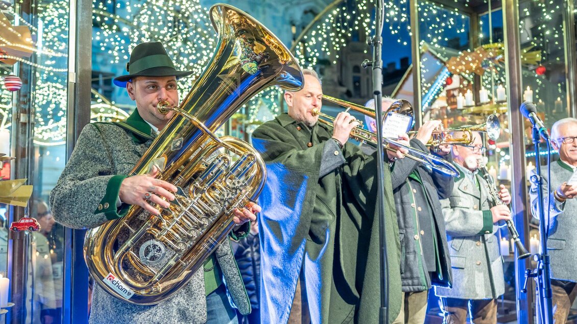 Eine Gruppe von Musikern spielt auf einem Weihnachtsmarkt. Lichter funkeln im Hintergrund und schaffen eine festliche Atmosphäre. | © Stadt Graz - Foto Fischer