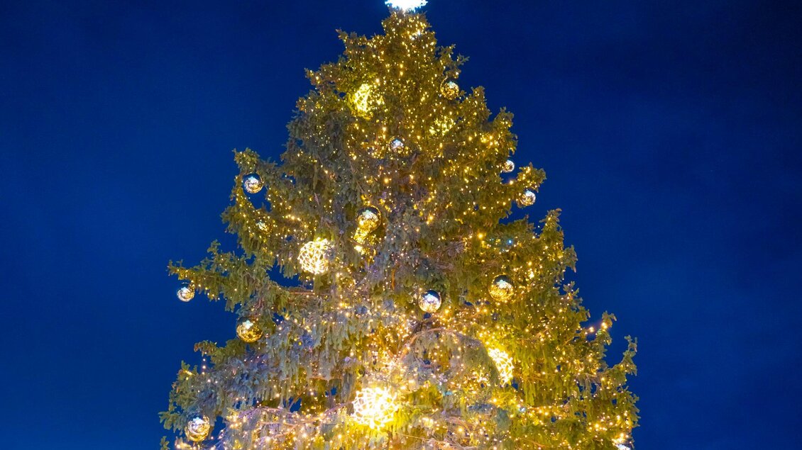 Ein festlich geschmückter Weihnachtsbaum mit strahlenden Lichtern und glitzernden Kugeln. Der Hintergrund ist ein klarer, dunkler Abendhimmel. | © Stadt Graz - Foto Fischer