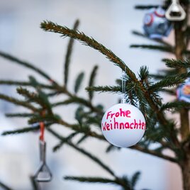 Ein geschmückter Weihnachtsbaum mit einer weißen Kugel, auf der "Frohe Weihnachten" steht. Im Hintergrund sind weitere Weihnachtsdekorationen zu sehen. | © TV MUrau