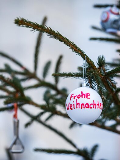 Ein geschmückter Weihnachtsbaum mit einer weißen Kugel, auf der "Frohe Weihnachten" steht. Im Hintergrund sind weitere Weihnachtsdekorationen zu sehen. | © TV MUrau