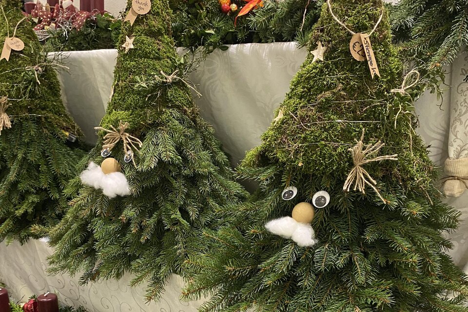 Drei dekorative Weihnachtsbäume aus Moos und Tannenzweigen stehen auf einem Tisch. Jeder Baum hat ein lustiges Gesicht mit einem weißen Bart und verschiedenen Anhängern. | © Eva-Maria Paier