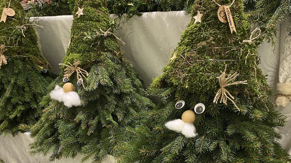 Drei dekorative Weihnachtsbäume aus Moos und Tannenzweigen stehen auf einem Tisch. Jeder Baum hat ein lustiges Gesicht mit einem weißen Bart und verschiedenen Anhängern. | © Eva-Maria Paier