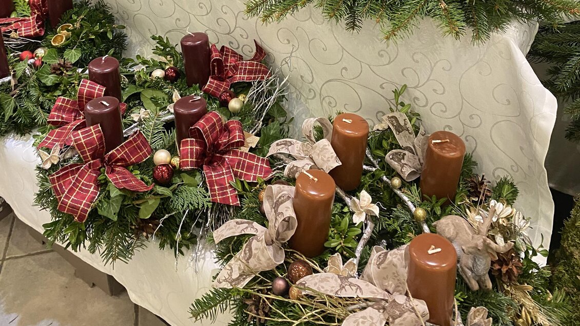 Dekorative Adventskränze mit Kerzen und Schleifen sind auf einem Tisch arrangiert. Die Kränze sind aus grünem Tannenzweigen mit rotem und braunem Farbakzenten. | ©  Eva-Maria Paier
