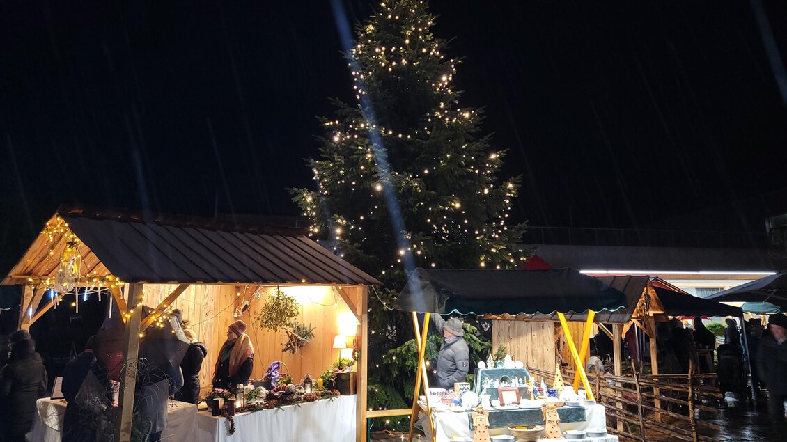 Ein festlicher Weihnachtsmarkt bei Nacht mit leuchtenden Ständen und einem großen, geschmückten Baum. Die Atmosphäre ist warm und einladend. | © Birgit Friedl