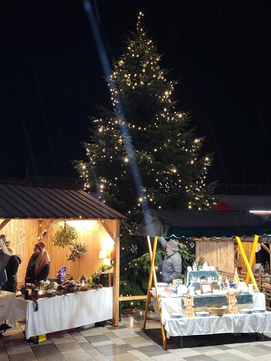 Ein festlicher Weihnachtsmarkt bei Nacht mit leuchtenden Ständen und einem großen, geschmückten Baum. Die Atmosphäre ist warm und einladend. | © Birgit Friedl