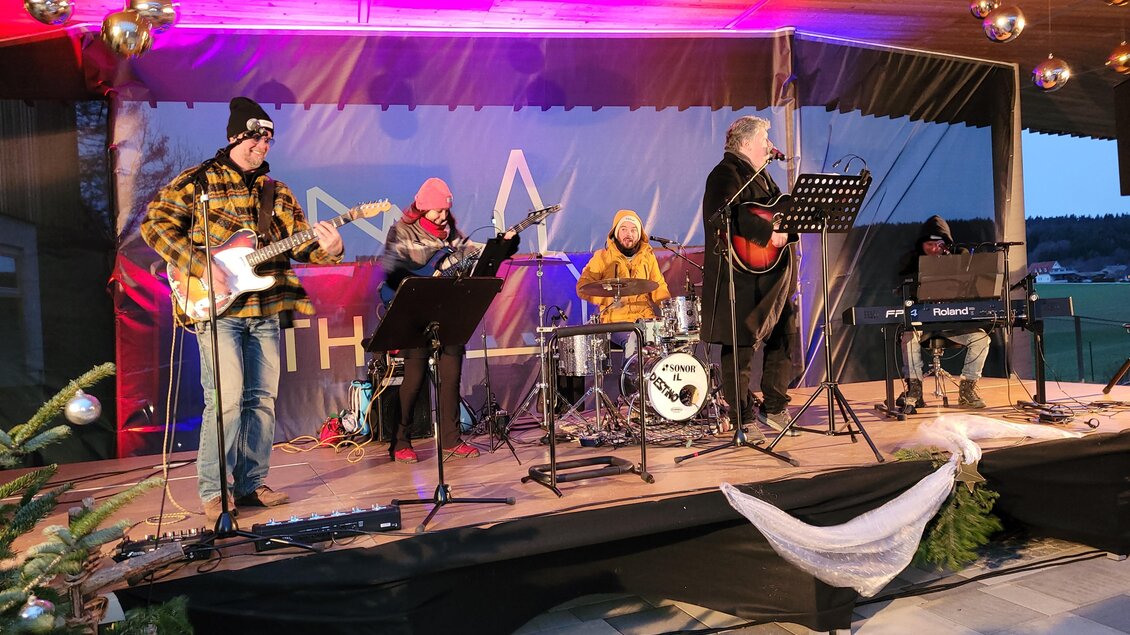 Eine Band spielt live auf einer Bühne. Die Musiker sind warm angezogen und es gibt festliche Dekorationen. | © Birgit Friedl